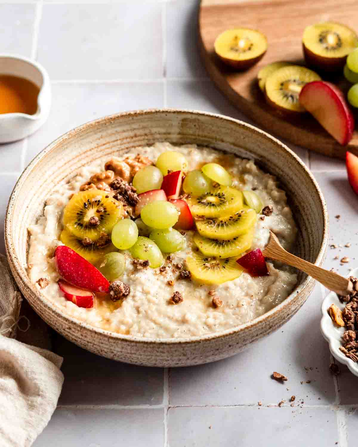 sorghum porridge in a bowl topped with fresh kiwis, plums, granola and maple syrup.