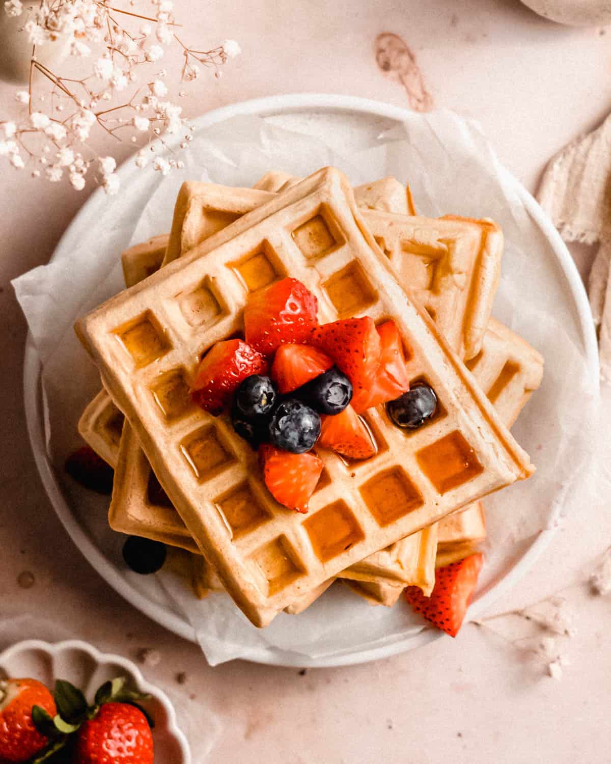 stack of waffles on plates topped with fresh fruits and maple syrup.