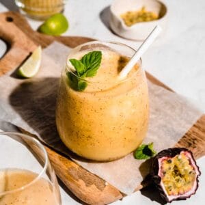 passion fruit smoothie topped with fresh mint on a wooden cutting board, next to it a passion fruit.