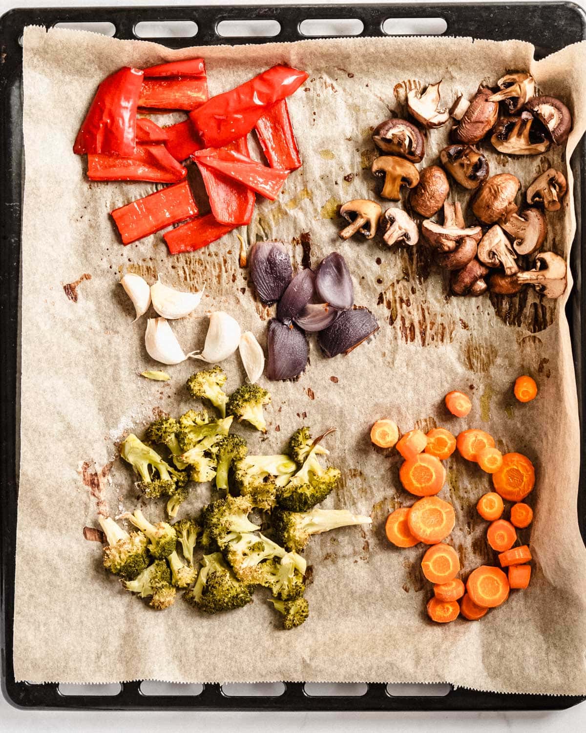 roasted chopped red bell pepper, brown mushooms, red onion, garlic with skin on, broccoli florets and carrot coins on a baking tray lined with parchment paper.
