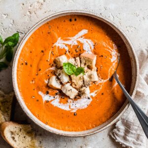 roasted cherry tomato soup in a soup bowl topped with bread croutons, black pepper and fresh basil.