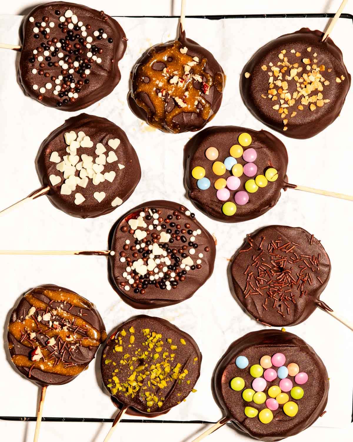Chocolate covered apple slices topped with different toppings on a wire rack covered with parchment paper.