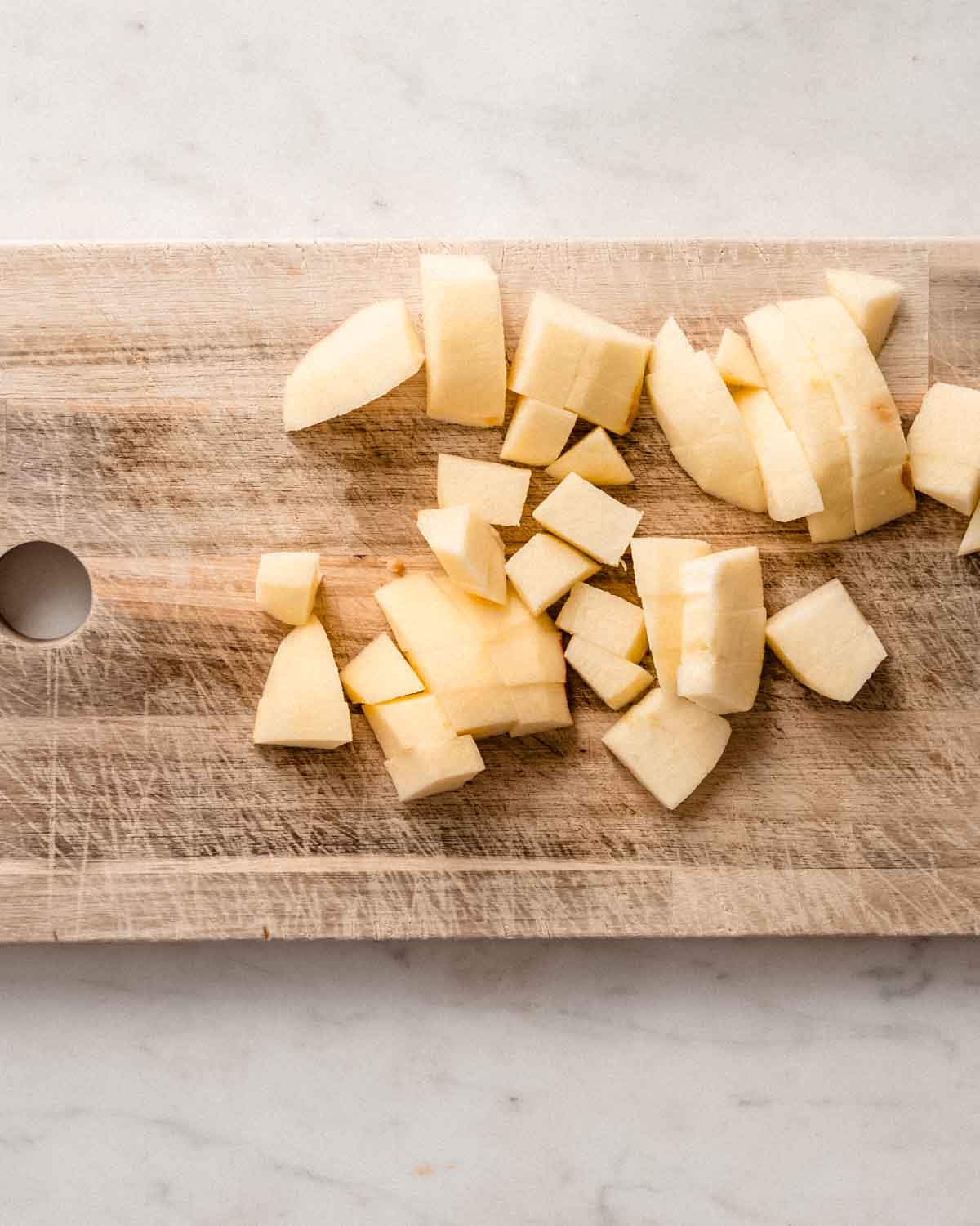 Peeled and chopped apple chunks on a wooden cutting board.