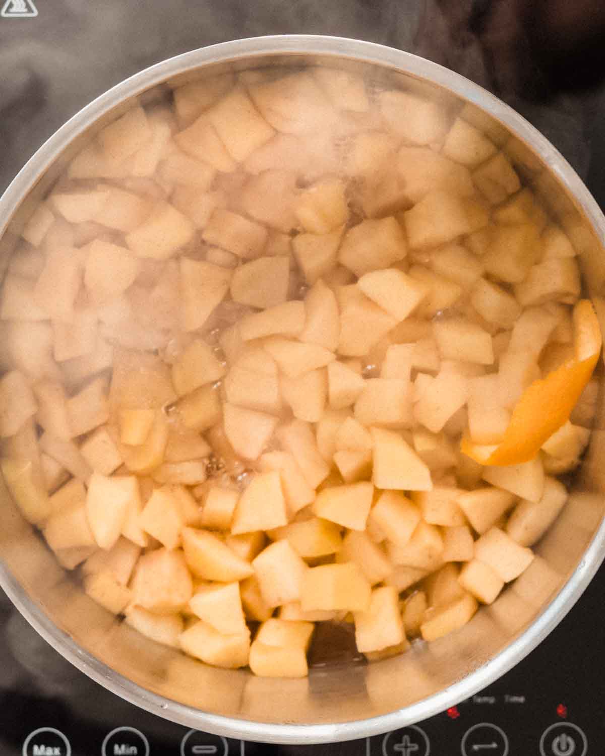 Apple chunks, cinnamon, water, orange peel and lemon juice simmering in a large pot.