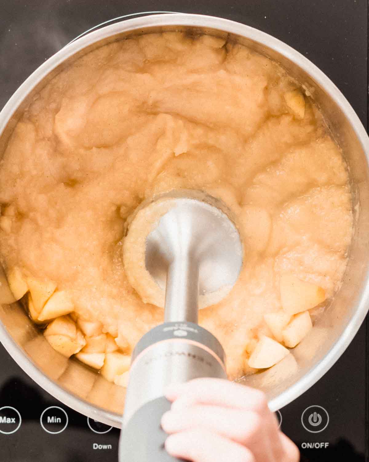 Cooked potato chunks being pureed in a saucepan with a stick blender.