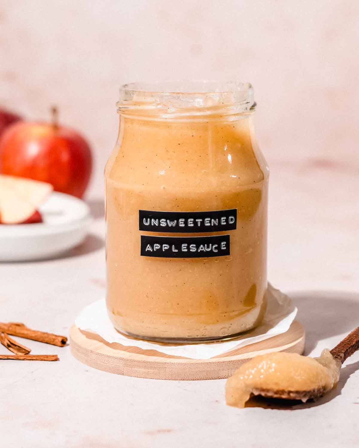 glass jar filled with unsweetened applesauce and a wooden spoon with applesauce on it next to it.