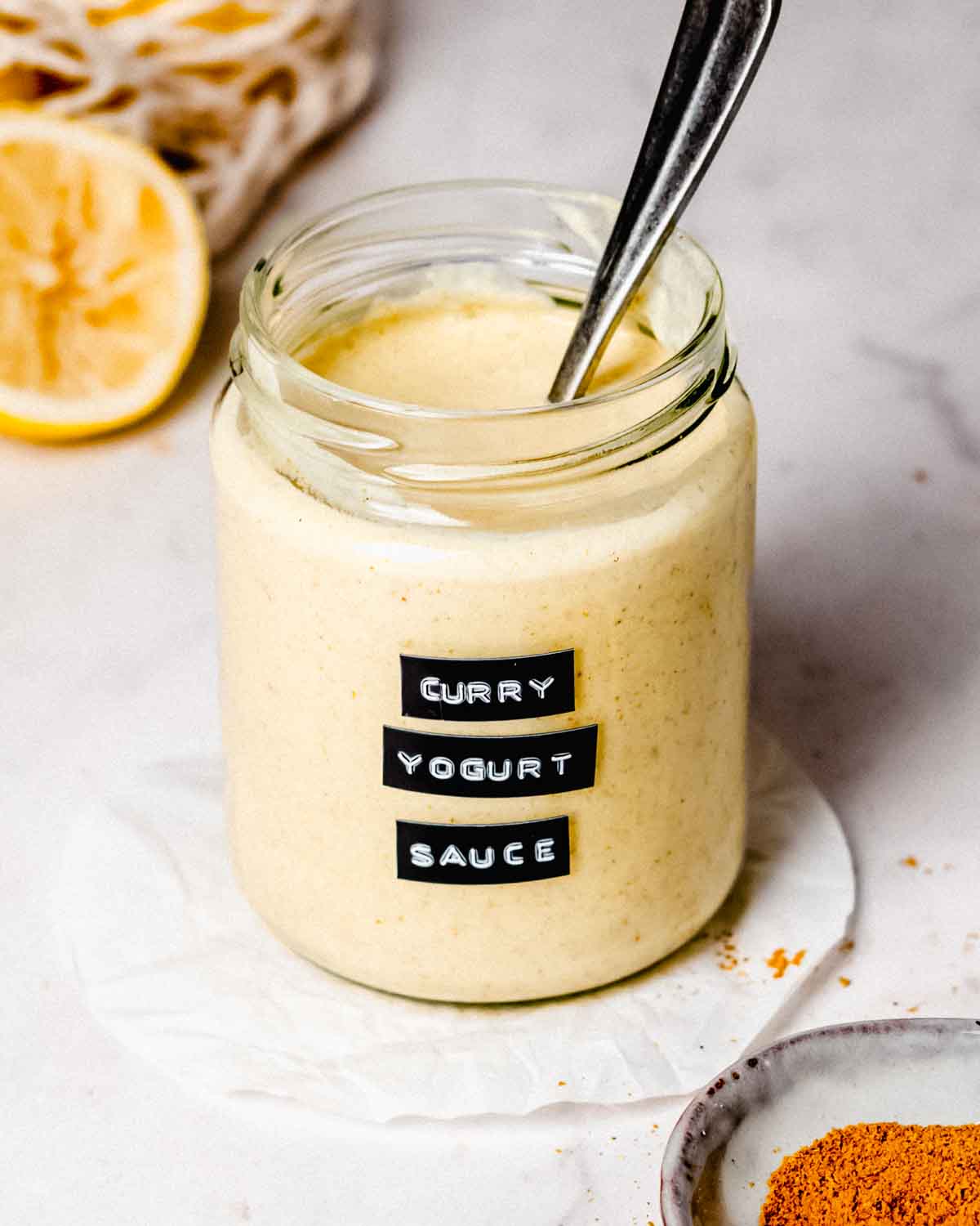 Curry yogurt sauce in a glass jar with a spoon.