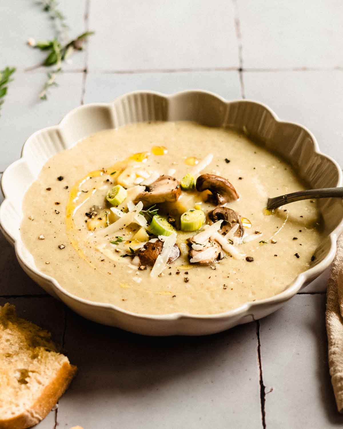 Ratatouille soup in a soup bowl garnished with fresh herbs, parmesan and olive oil. Next to it fresh herbs and white bread.