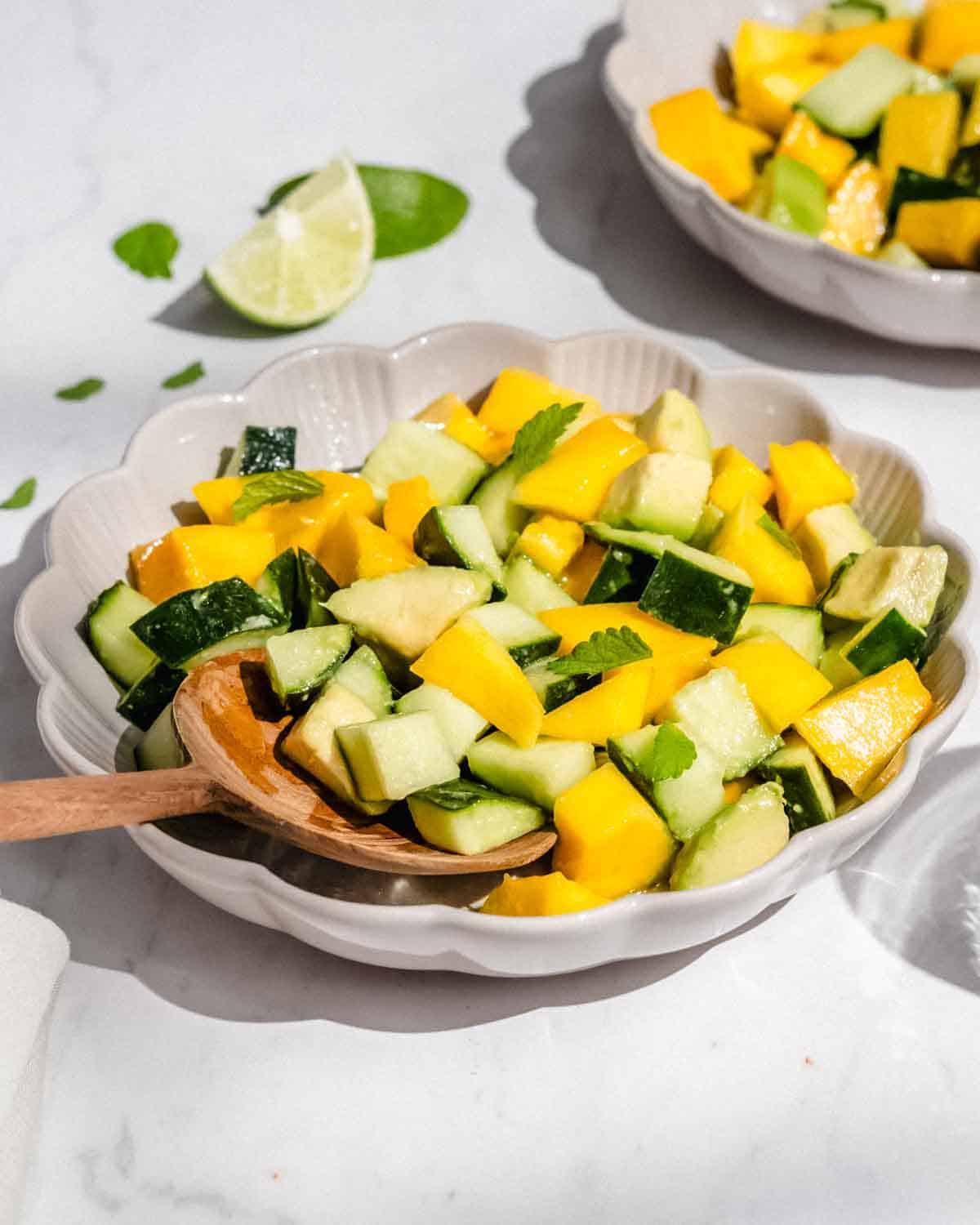 2 bowls of mango avocado salad in small bowls. Next to it fresh lime wedges and mint leaves.