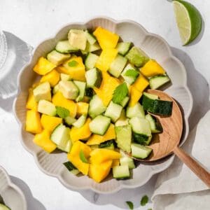 close up of mango Avocado Cucumber Salad in a small bowl. Next to it fresh lime wedges.