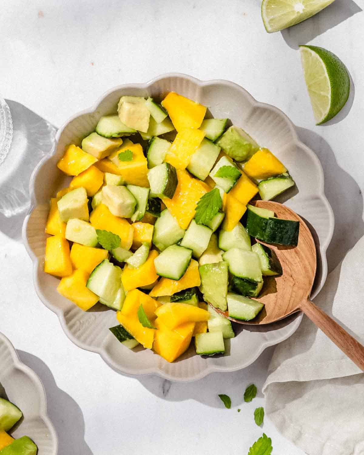 Mango Avocado Cucumber Salad in a small bowl. Next to it fresh lime wedges.