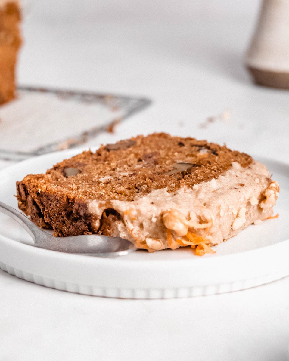 1 slice of carrot cake on a small plate with a spoon next to it.