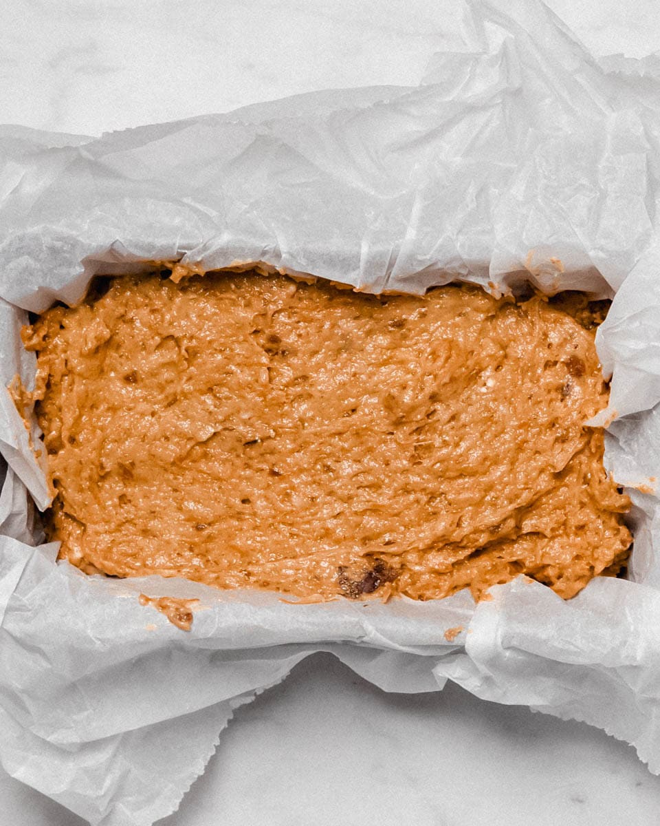 Cake dough in a loaf pan lined with parchment paper, ready to bake.