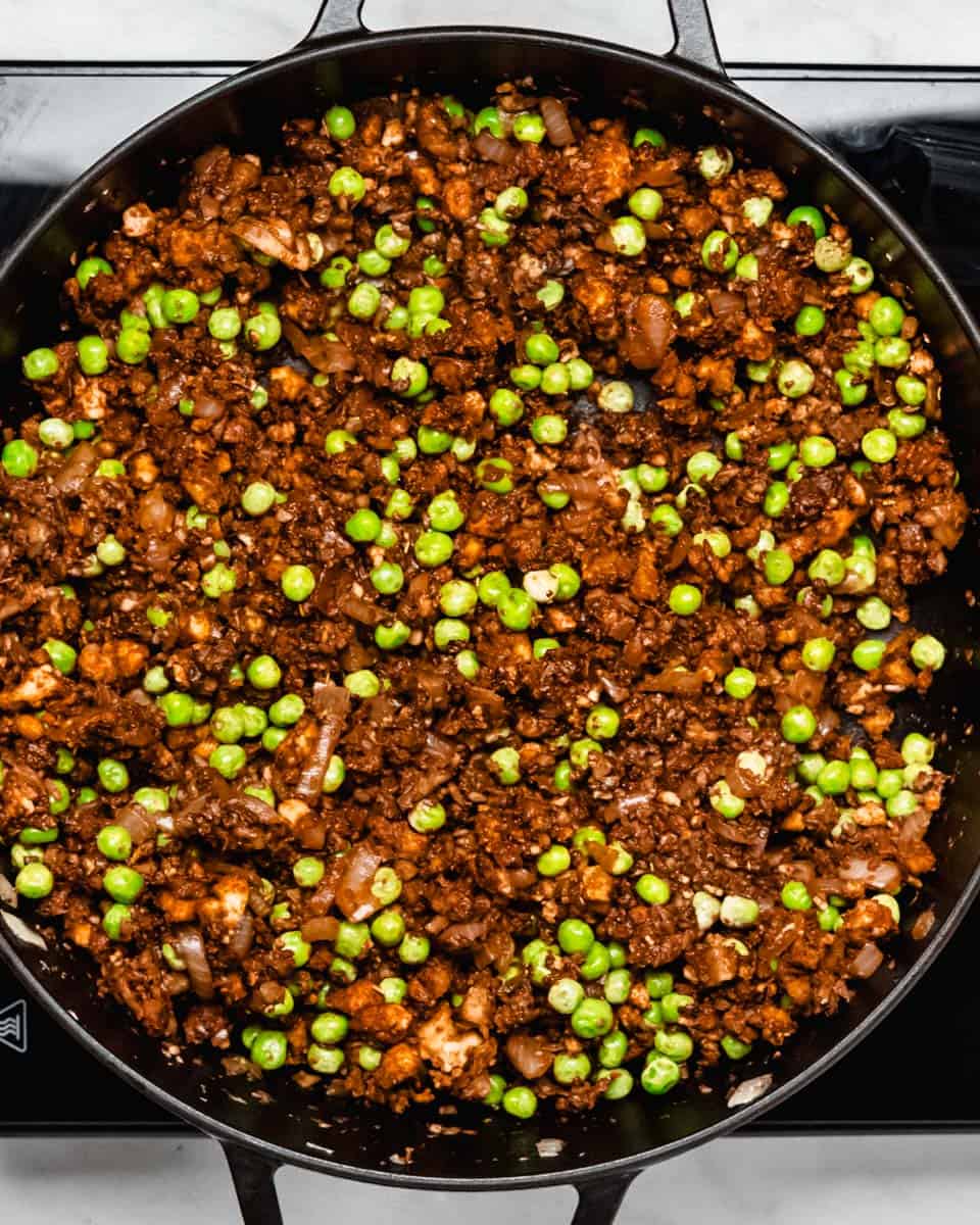 Sauteed mushrooms, tofu crumbles and frozen peas in a skillet.