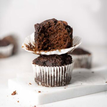 2 chocolate veggie muffins stacked onto each other on a marble white plate. One bite bitten off the one on the top.