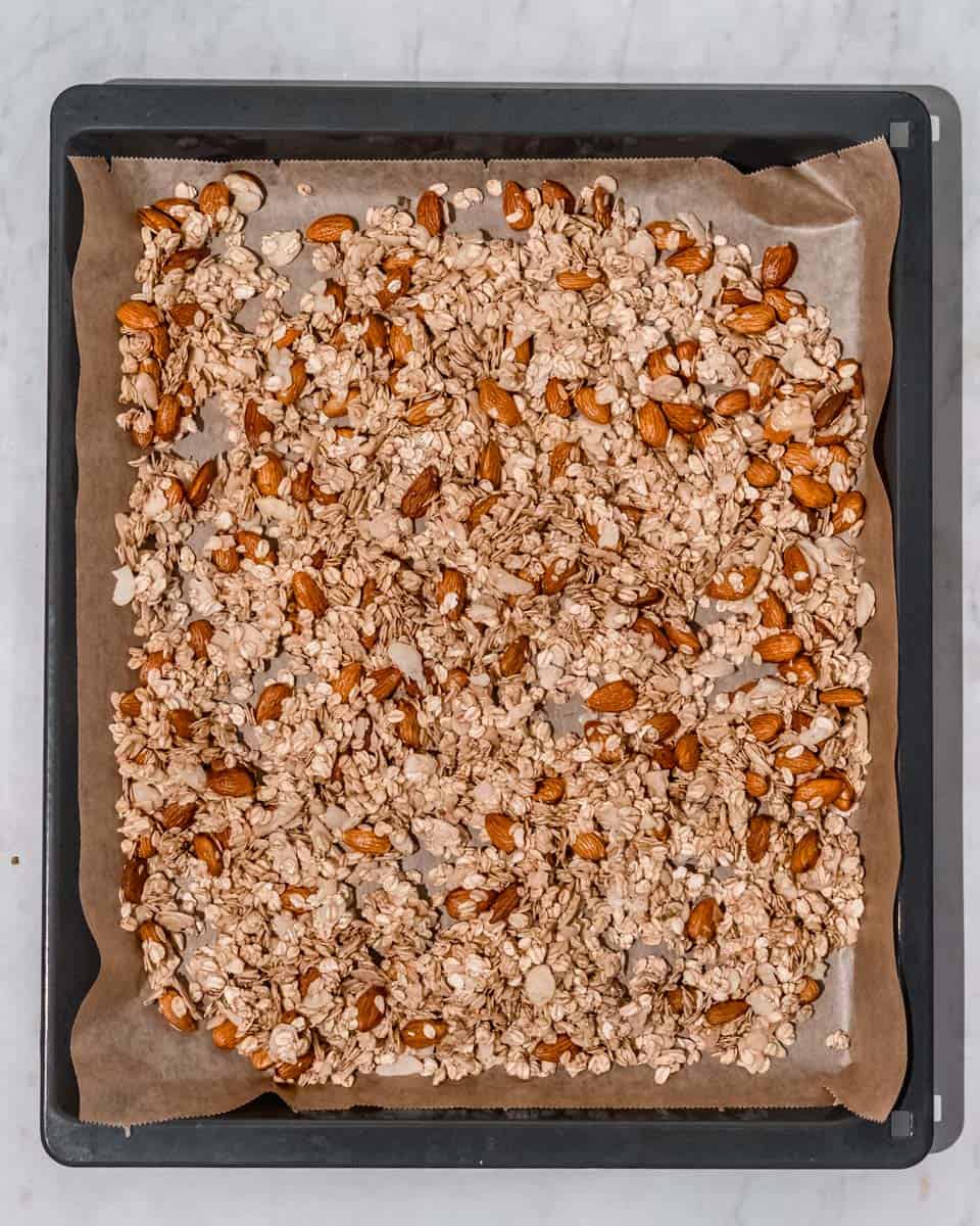 Vanilla almond granola spread out on a baking sheet lined with parchment paper ready to be baked.