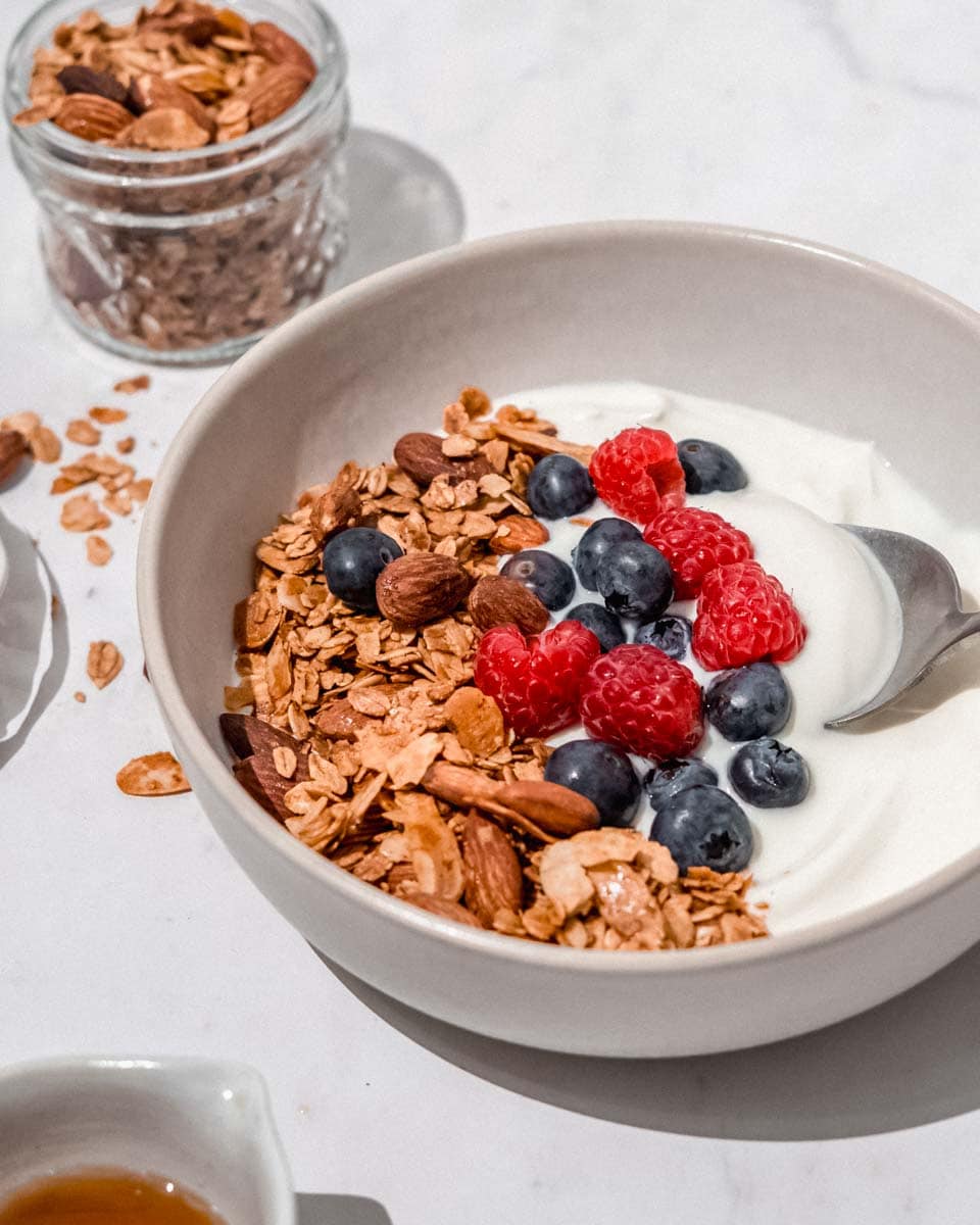 A bowl filled with Greek yogurt, vanilla almond granola and fresh raspberries and blueberries.