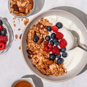 Birdseye view of a bowl filled with Greek yogurt, vanilla almond granola and fresh raspberries and blueberries.