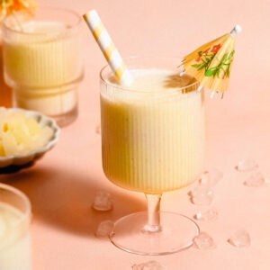 Three glasses of piña colada smoothie, with the center glass garnished with a straw and a cocktail umbrella.
