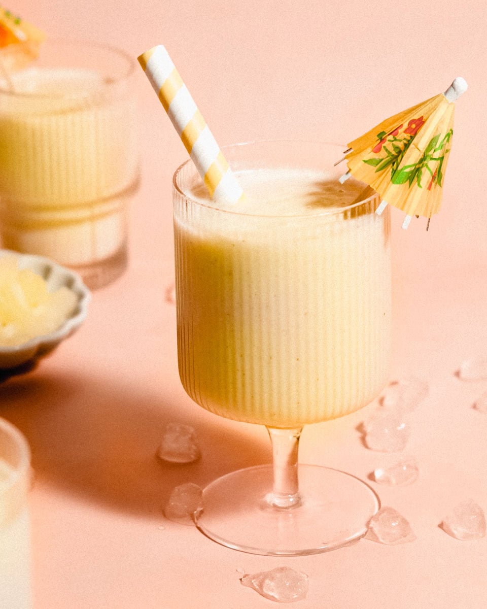 Three glasses of piña colada smoothie, with the center glass garnished with a straw and a cocktail umbrella.
