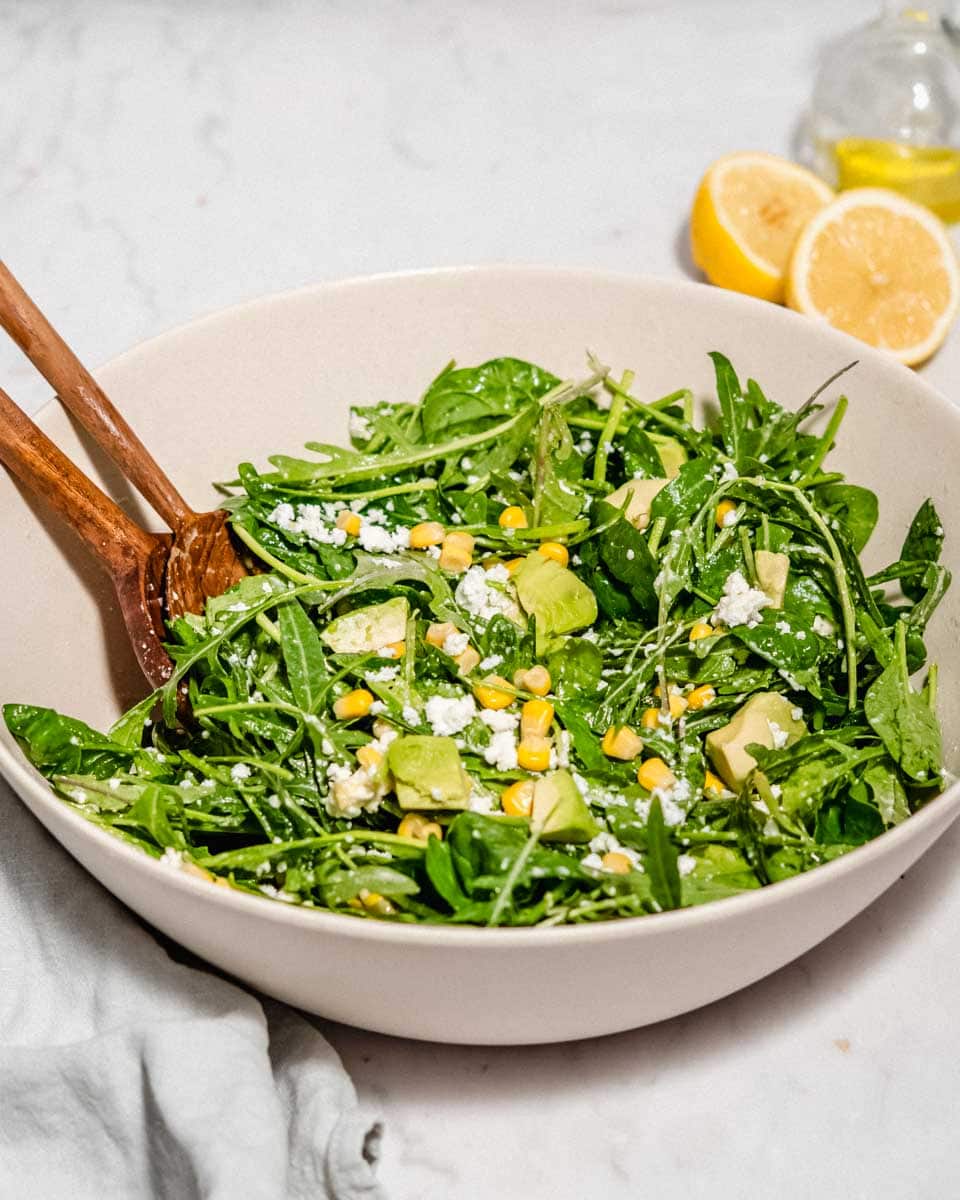 Spinach Arugula salad in a large bowl. Behind some fresh lemons and olive oil.