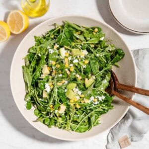Birds-eye-view of arugula spinach salad in a large bowl with a big wooden spoon and fork in it.