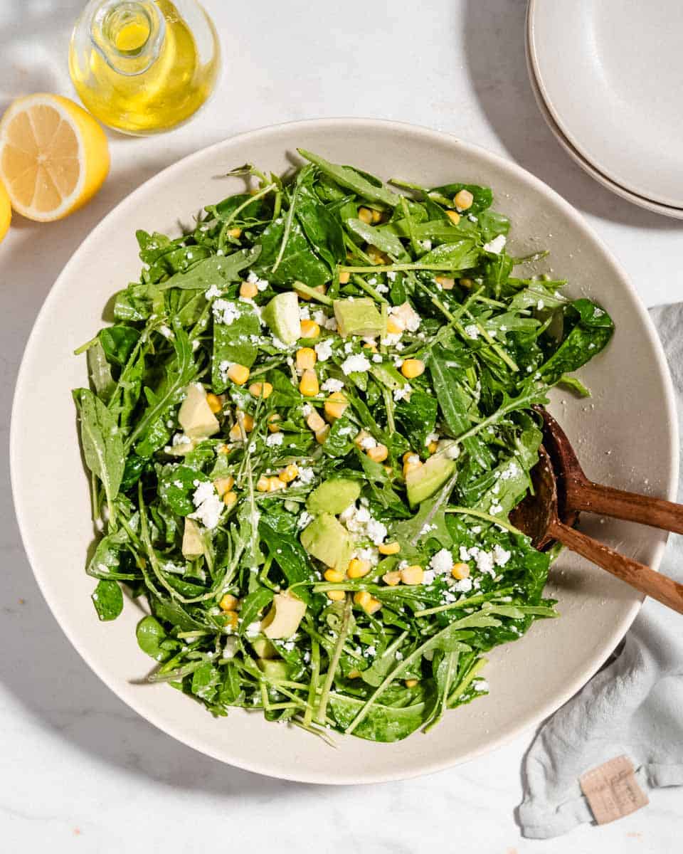 Birds-eye-view of arugula spinach salad in a large bowl with a big wooden spoon and fork in it.