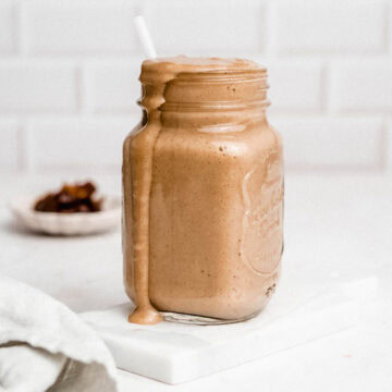 Banana date smoothie in a glass jar with a straw, a little drizzle running down the side.