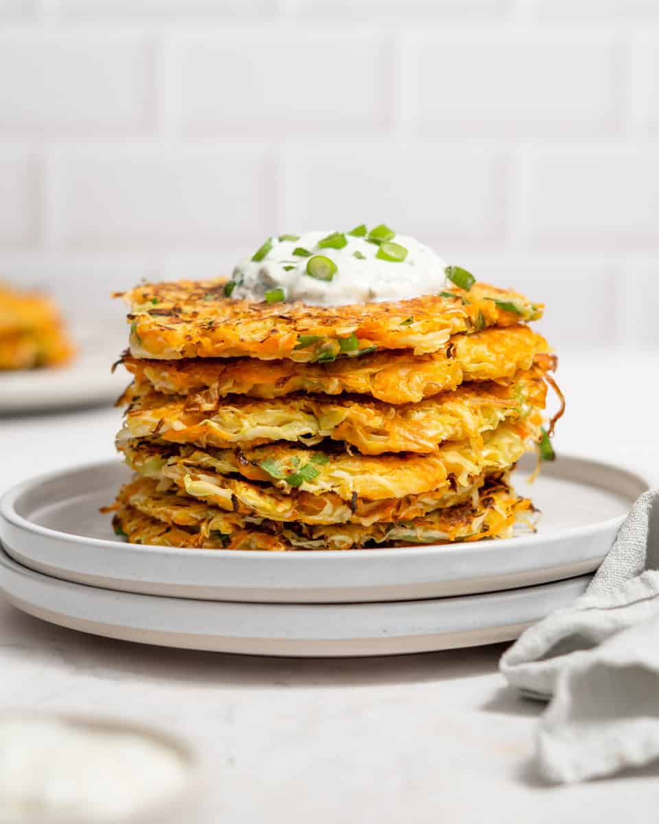 Stack of 6 cabbage fritters on two plates topped with a yogurt dip.