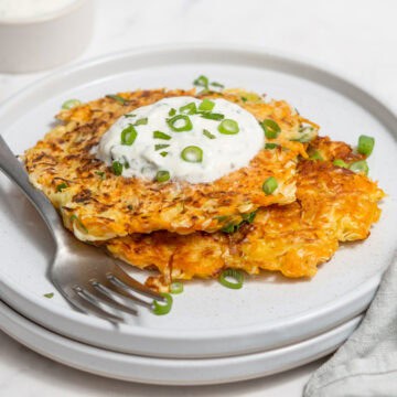 Two cabbage fritters on a plate topped with a yogurt dip and scallions and chives.