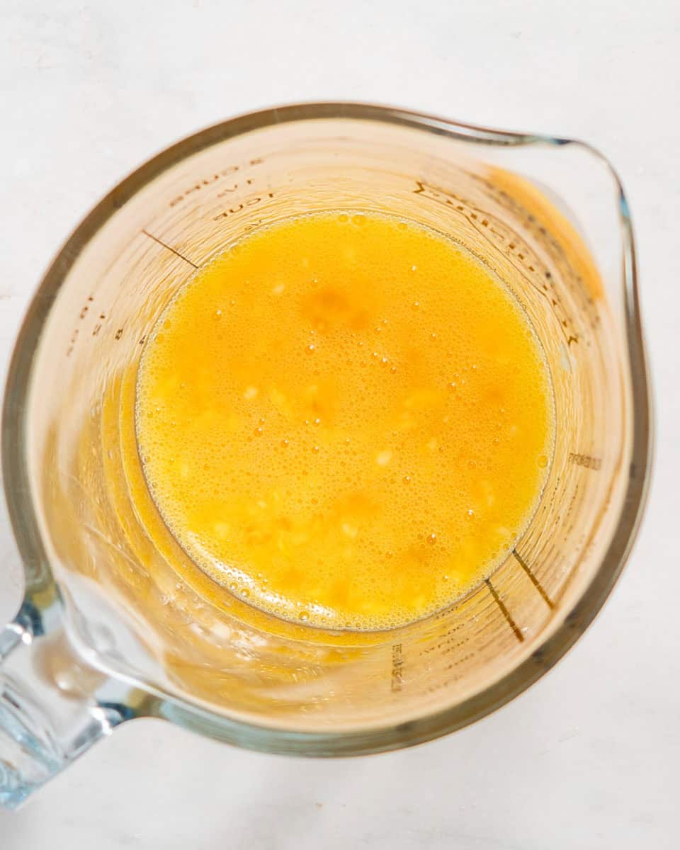 Eggs whisked together with minced garlic and salt in a glass jug.