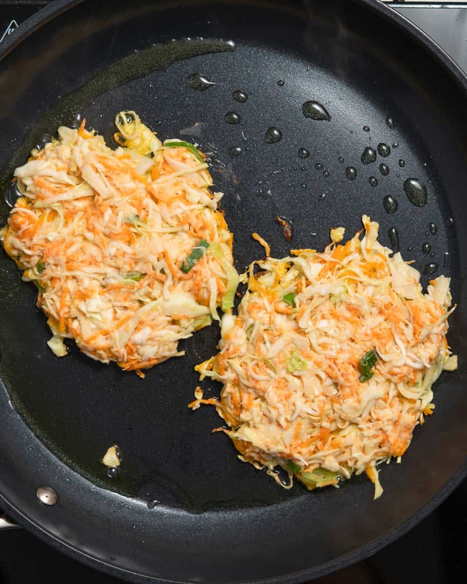 2 cabbage fritters frying in a pan.