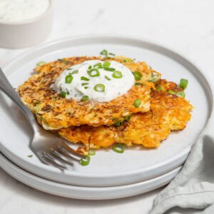 Two cabbage fritters on a plate topped with a yogurt dip and scallions and chives.