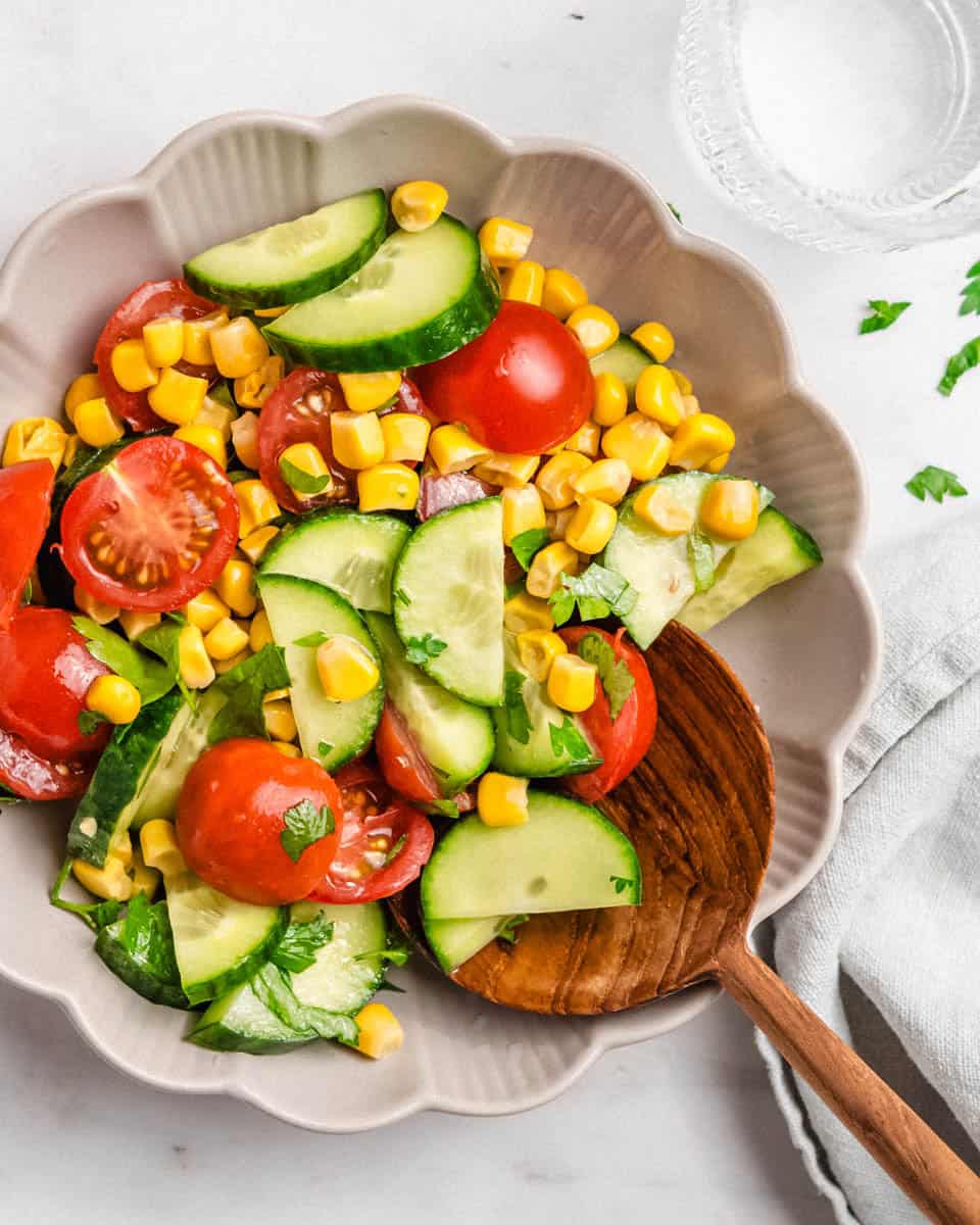 Birds-eye-view of this salad in a bowl. Next to it a glass of water and a linen napkin.