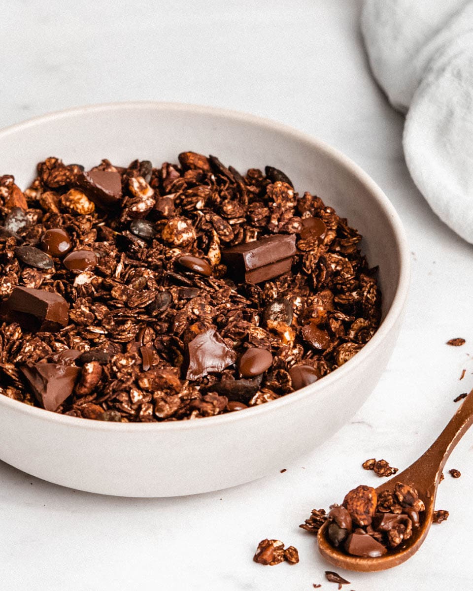 Dark chocolate granola in a bowl, in the front of it a spoon full of granola.
