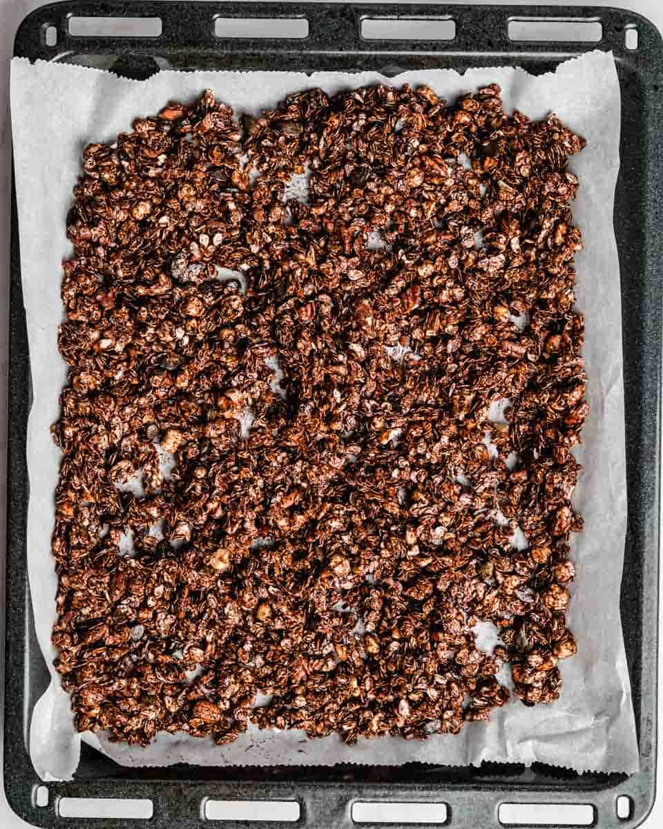 Chocolate granola spread out on a baking tin lined with pachment paper.