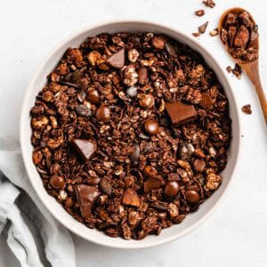 Bird's eye view of dark chocolate granola in a bowl, next to it a spoon full of granola.