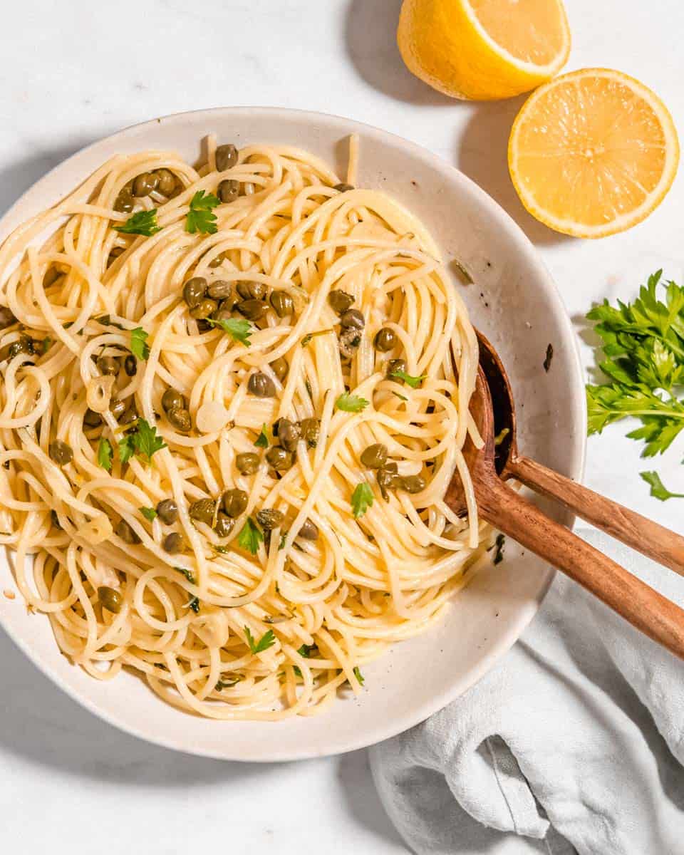 Bird's eye view of a lemon caper pasta on a pasta plate topped with fresh parsley. A lemon and a glass of water next to it.