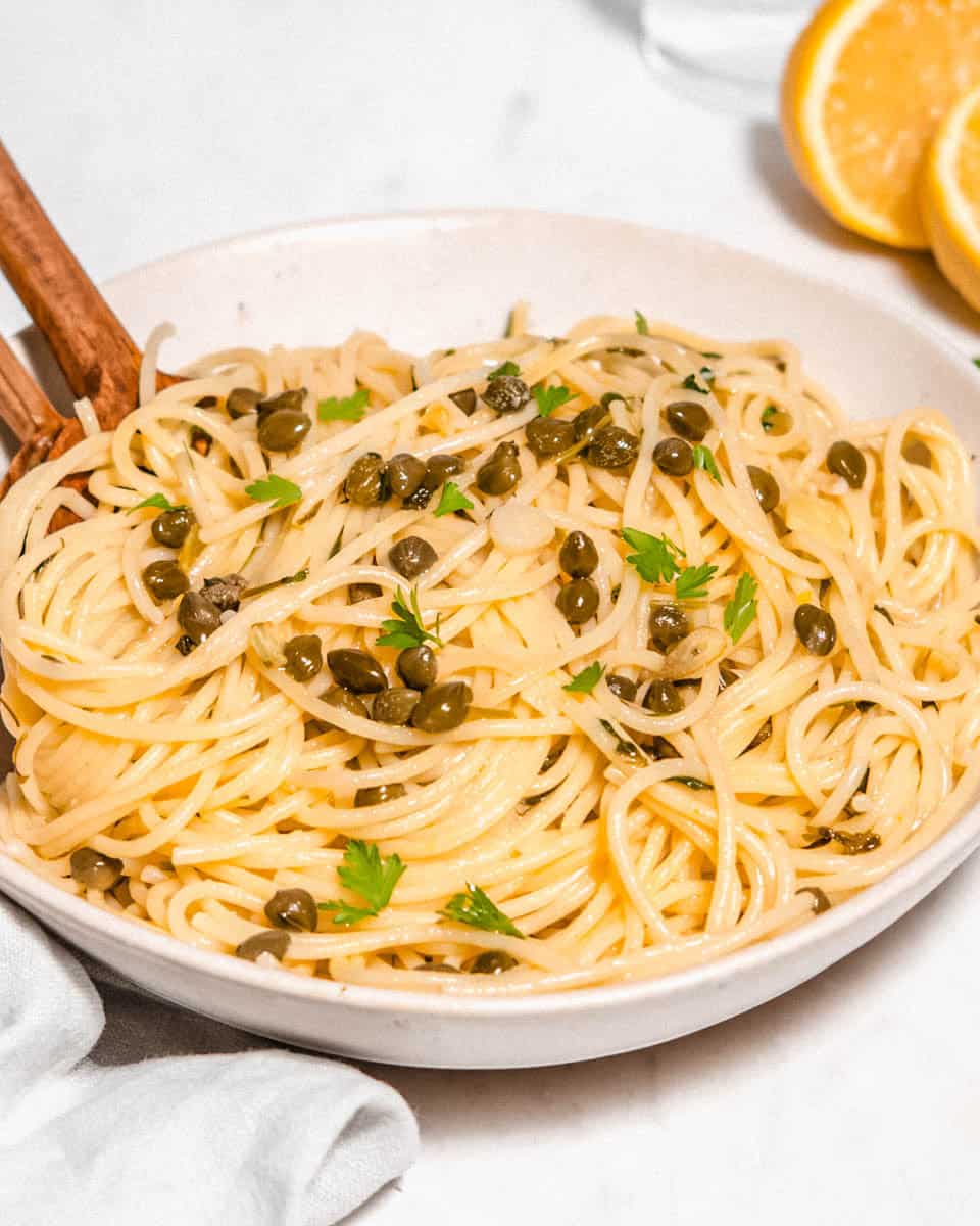 Bird's eye view of a lemon caper pasta on a pasta plate topped with fresh parsley. A lemon and a glass of water next to it.