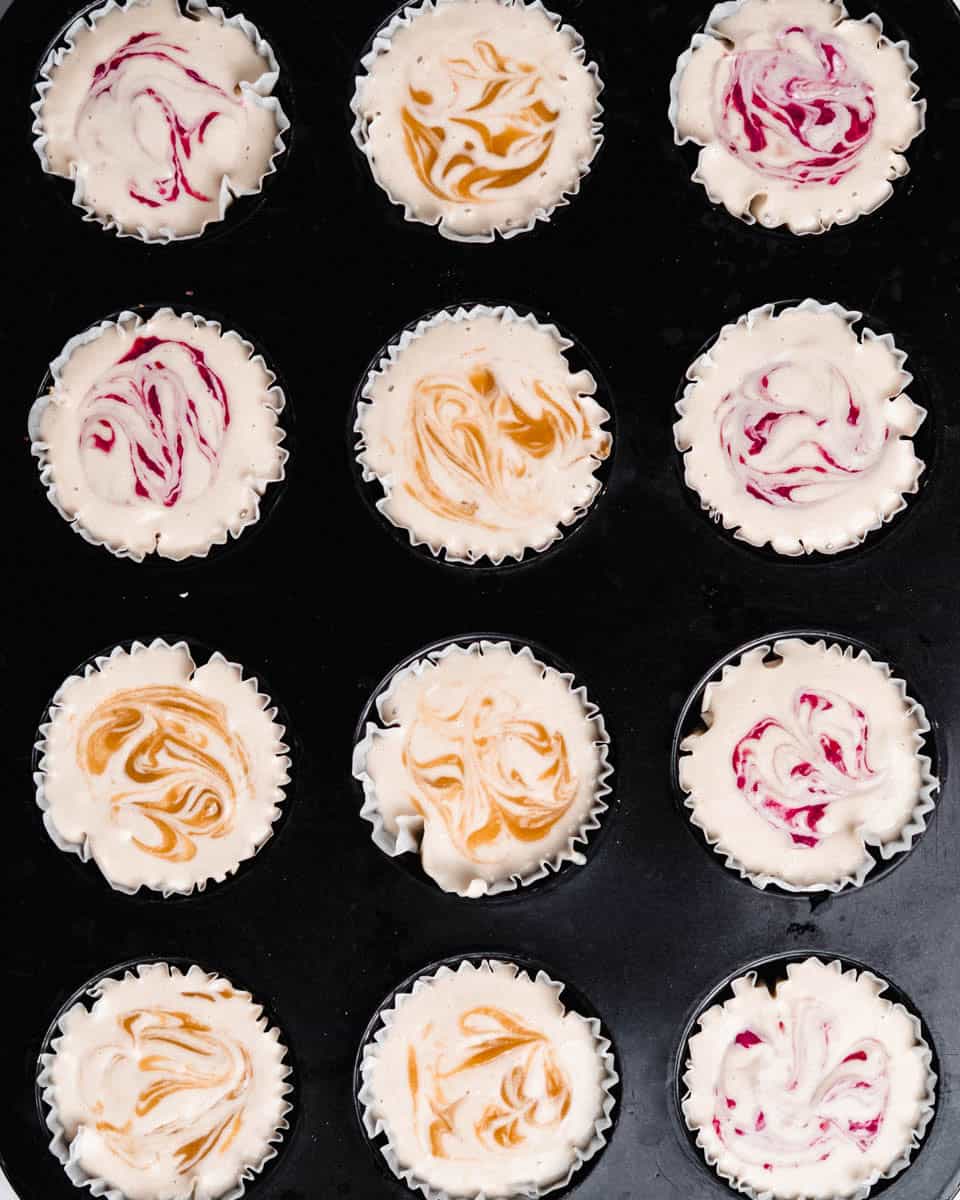 12 cheesecakes in a muffin tin, ready to be put in the freezer.