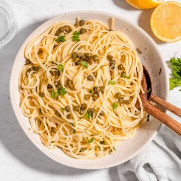 Bird's eye view of a lemon caper pasta on a pasta plate topped with fresh parsley. A lemon and a glass of water next to it.