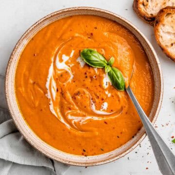 Creamy pumpkin tomato soup topped with coconut milk swirls, red pepper flakes, and a fresh basil leaf.