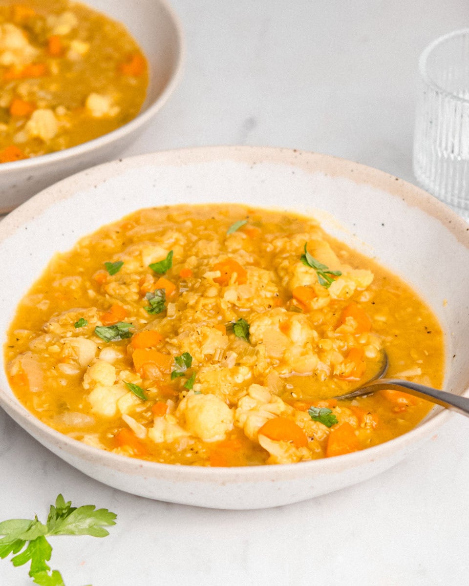 2 bowls of cauliflower lentil soup in a bowl with a spoon topped with fresh herbs.