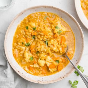 Birds-eye view of cauliflower lentil soup in a bowl with a spoon topped with fresh herbs.