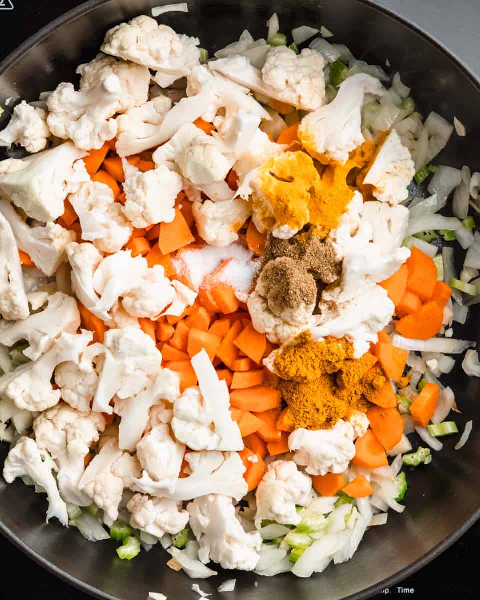 Cauliflower florets, diced carrots and spices added to the onion-garlic-celery mix in a pan.