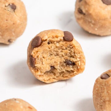 A close-up of a cookie dough protein ball with a bite taken out, showing its soft, chewy texture inside.