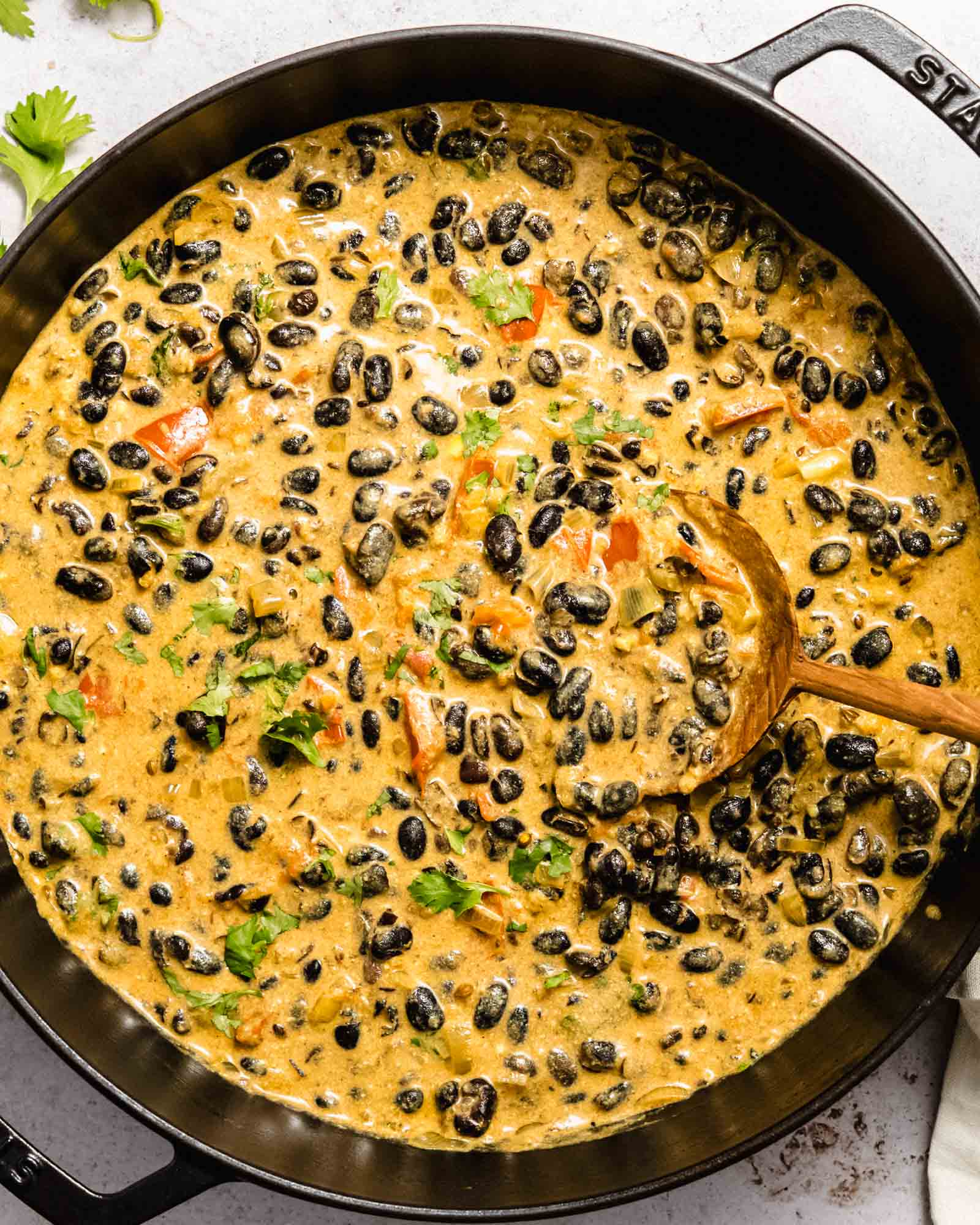 Birds eye view of a bean curry in a large saucepan with a wooden spoon in it.