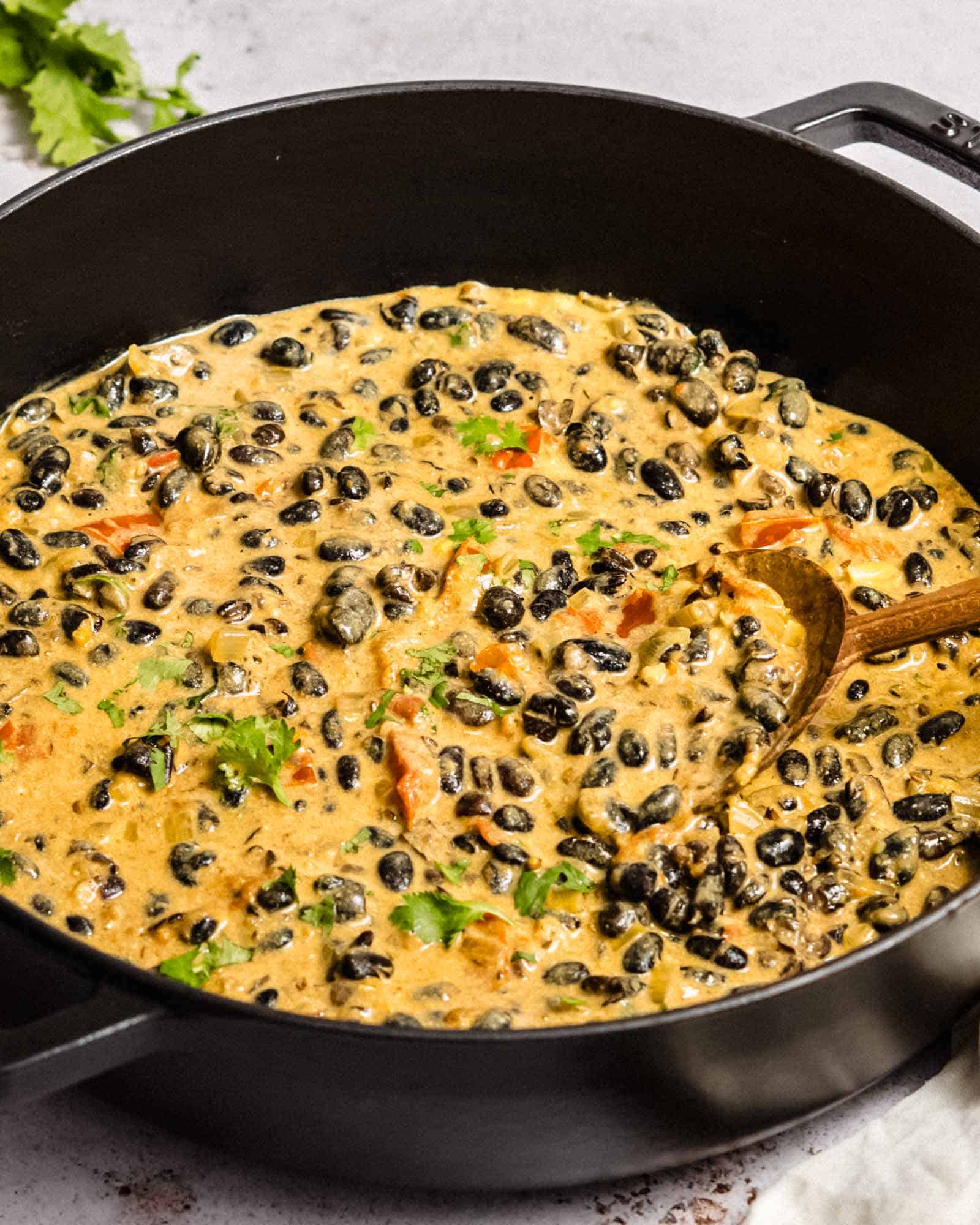 Bean curry in a large saucepan with a wooden spoon in it.