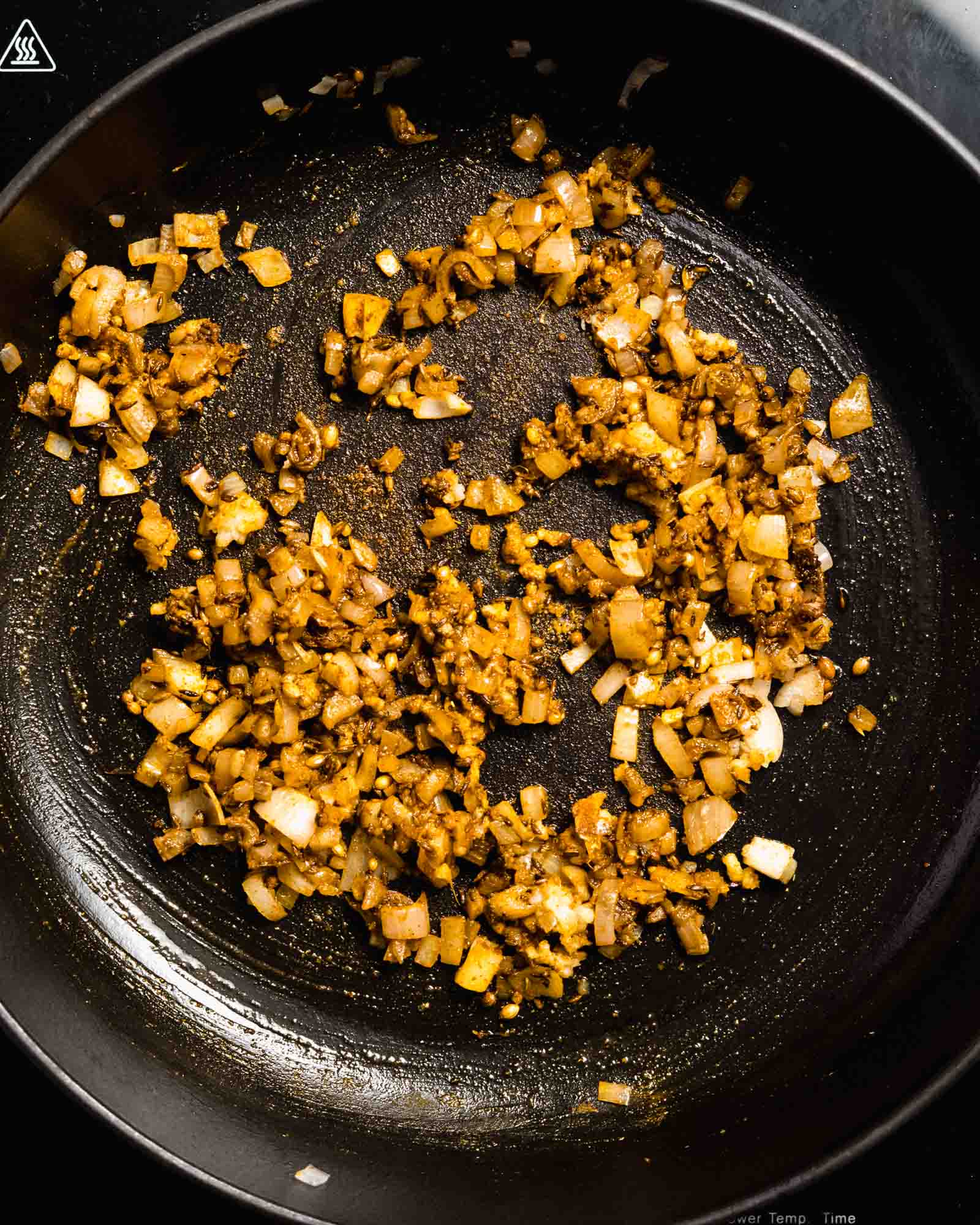 Fried onion, cumin and coriander seeds and spices in a pan.