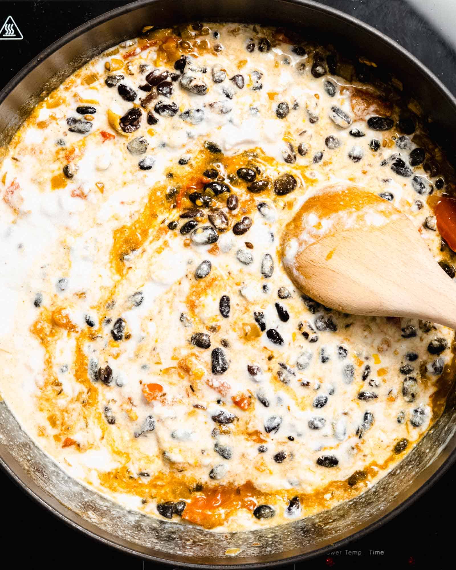 Coconut milk and black beans added to the base ingredients in a pan.